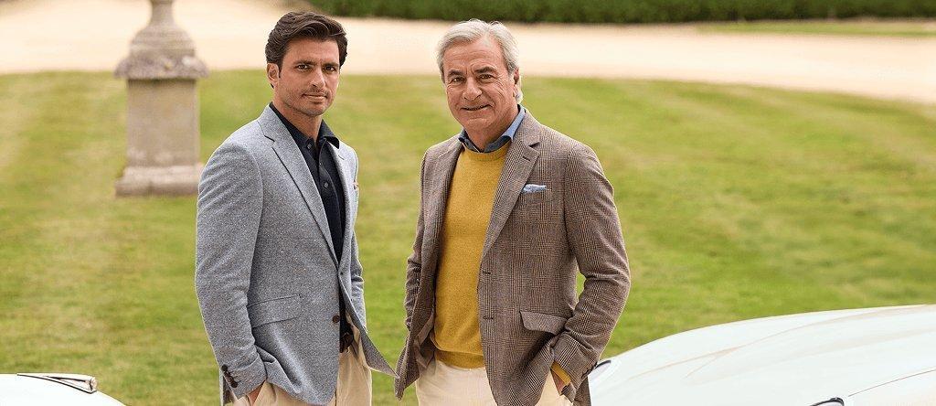 Two men wearing Hacketts London suit jackets and smart trousers in front of car and grass background.